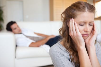woman upset while husband is on the couch behind her
