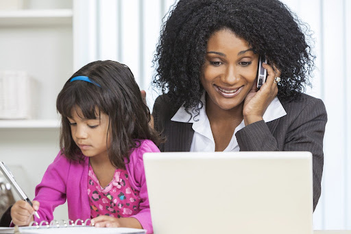 Businesswoman speaking on the phone, looking at a laptop computer screen, with a small child on her lap; custody battles in high net worth divorces can present challenges in balancing wealth and parental rights.