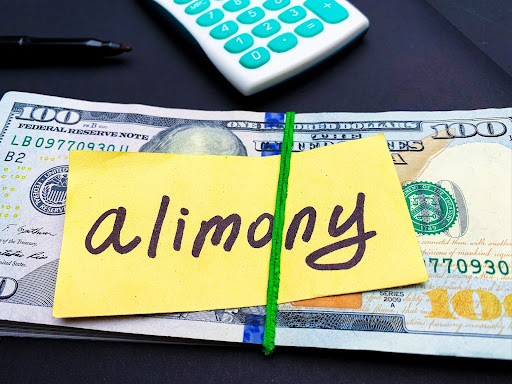 A stack of paper money is contained in a rubber band with a yellow sticky note with the word “alimony” written on it. Spousal support in high net worth divorces can be a little more complicated.