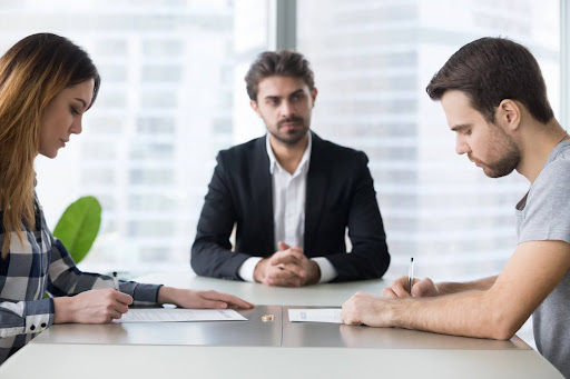 A mediator helping a man and a woman sign legal agreements regarding blended families and court mediation.